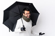 © luismolinero - Caucasian handsome man with beard holding an umbrella over isolated white wall smiling