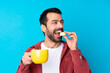 © luismolinero - Young caucasian man over isolated blue background holding colorful French macarons and a cup of milk