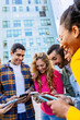 © Xavier Lorenzo - Diverse student group hanging out in city park using mobile phones. Multiracial young friends enjoying social media on cellphones outdoors. Technology and youth lifestyle concept