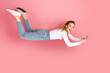 © deagreez - Cheerful young woman floating effortlessly on pink background holding smartphone showcasing playful and innovative casual lifestyle