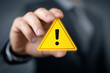 © iconic - A hand prominently holds a bright yellow warning triangle symbol.