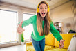 © deagreez - Cheerful young woman in a green sweatshirt enjoying music indoors with bright yellow headphones in a stylish loft apartment