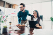 © deagreez - Two colleagues in a modern loft office collaborate over charts and a clipboard during a busy business meeting