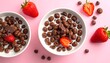 © Comben - Two bowls of chocolate cereal, milk, strawberries on pink background, overhead