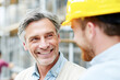 © Kowit - Two men smile and engage in conversation at a construction site, showcasing a positive and friendly work environment.