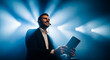 © Miftakhul - Smiling businessman with headset and tablet on stage under spotlights, presenting, live event, speaker.