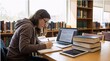 © riddler - Young woman studying with laptop and books in a library.