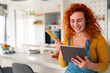 © Dorde - Smiling young red haired woman cooking breakfast in bright modern kitchen using tablet