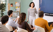 © JackF - In lesson, Asian girl teacher tell material and gives lecture, speaks to group of students. Students taking trial class in language courses, acting school. Group lessons at school of foreign languages
