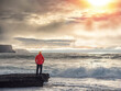 © mark_gusev - Tourist in red jacket is standing on a small rock with spectacular nature scenery with cliff, ocean and dramatic sky in the background. Doolin, area, Ireland. Travel and tourism.