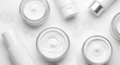 © Dhinaa - Top view of various white cosmetic cream jars and lotion bottles neatly arranged on a pristine white background, showcasing essential skincare and beauty products