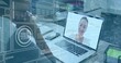© vectorfusionart - Smiling woman appearing on open laptop screen with HUD at desk, wearing blouse with smartphone