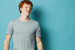 © SHOTPRIME STUDIO - Young man with red hair smiling and wearing gray t shirt against blue background in studio. Casual portrait of happy male model with light skin and short hairstyle.