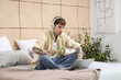 © Pixel-Shot - Young handsome man in headphones with disposable electronic cigarette using laptop on bed at home