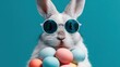 © mila103 - Trendy rabbit wearing sunglasses holding colorful easter eggs.