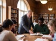 © Meow Creations - Senior professor helping diverse college students study in a traditional university library hall