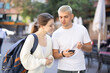 © JackF - On pedestrian street, guy and girl are looking at smartphone screen, ordering taxi. Tourists use international taxi aggregator to call car..