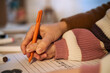© DragonImages - Caucasian child practicing handwriting with orange pen, small hand gripping writing instrument while tracing letters on worksheet, adult hand gently guiding movement, close up view