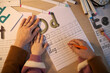 © DragonImages - Caucasian woman guiding Caucasian child writing letters on worksheet, adult hand helping child hand form letters, educational activity involving handwriting practice at desk