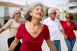 © Anna Lurye - Cheerful senior hispanic woman dancing salsa with friends in a sunny outdoor plaza representing active aging and social joy