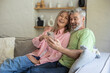 © zinkevych - Senior couple sitting on sofa using smartphone together in living room