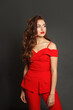 © artmim - Glamorous young woman in red suit standing against black studio wall background