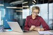© Liubomir - Young woman wearing headphones and glasses, watching webinar on laptop, writing notes in a notebook, studying or working remotely in a modern office setup