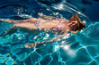 © Connect Images - Woman in floral bikini and sunhat floats joyfully on bright blue pool water. USA