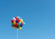 © Chanchai - A bright cluster of colorful helium balloons floating gently against a clear blue sky background, symbolizing joy, freedom, and festive cheer ,gas ,glossy ,reflective