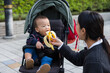 © leungchopan - Mother feeding baby banana on stroller outdoors