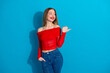 © deagreez - Stylish young woman in a red top and jeans posing confidently against a vibrant blue background with a cheerful smile.
