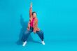 © deagreez - mature woman in pink top and fuzzy coat jumps with one finger raised in bright blue studio background