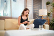 © Stella 16 - Smiling relaxed young woman sitting on couch using cell phone technology, happy lady holding smartphone, scrolling, looking at cellphone enjoying doing online e commerce shopping in mobile apps