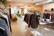© Marci - Bright modern clothing boutique with wooden floors, lush plants and neatly arranged racks of casual fashion creating a relaxed, welcoming shopping atmosphere