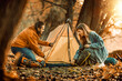 © ivanko80 - Couple sets up a tent in the woods during autumn with sunlight shining through trees in the late afternoon