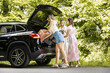 © ivanko80 - Three women loading bags into a car trunk in a green park on a sunny afternoon during summer