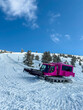 © DSMT - Snow groomer works on slopes at ski resort during winter season on sunny day with clear blue sky and mountain backdrop