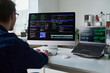 © Mediaphotos - Young man working at desk using desktop computer and laptop displaying programming code, sitting in office environment, focusing on software development tasks
