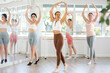 © JackF - Graceful young woman in sportswear confidently leading ballet class with female amateur dancers following her movements in spacious serene dance studio