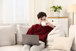 © New Africa - Man with cup of hot drink using laptop on sofa at home. Space for text
