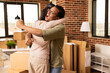 © DC Studio - Caucasian girlfriend and African American boyfriend celebrating with hug in new apartment. Happy diverse couple embracing joyfully after completing purchase of modern residential property.