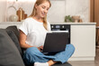 © brizmaker - Woman using a laptop in a modern apartment for online tasks