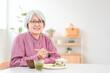 © buritora - A gray-haired senior woman eating in the dining room at home