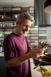 © Davor - Smiling mature man using smartphone while cooking in home kitchen