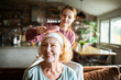 © Geber86 - Senior woman with face mask as younger woman brushes hair at home