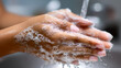 © Kanomaoi - Close up of hands lathered with white soap under running water from faucet
