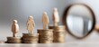 © Mia - Concept photo illustrating gender pay gap. Figurines stand atop stacks of coins, woman on top, men below. Magnifying glass explores income disparity in business, finance, economics. Equality, wage