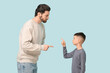 © Pixel-Shot - Young father and his little son pointing at each other while squabbling on blue background