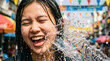 © Kos - Happy young Asian woman laughing as water splashes on her face. A joyful moment during the Songkran water festival in Thailand. Summer fun and celebration