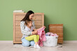© Pixel-Shot - Young woman and her daughter sort through fresh laundry near green wall at home